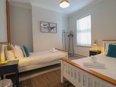 A bedroom with two single beds with folded towels on them bedside tables with lamps a window with blinds and two whale pictures on the wall at First Light in Pakefield near Lowestoft
