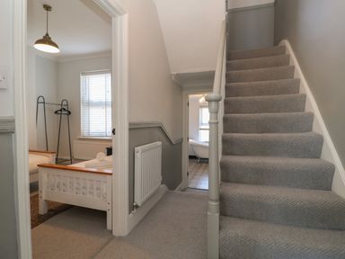 A hallway with carpeted stairs a bedroom with a bed and clothes rack and a bathroom with a clawfoot tub at First Light in Pakefield near Lowestoft