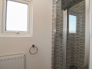 A bathroom with a window radiator towel ring and a shower with glass doors and tiled walls at First Light in Pakefield near Lowestoft