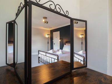 A bedroom with a metal bed frame white linens towels on bed and a black three-panel mirror at First Light in Pakefield near Lowestoft