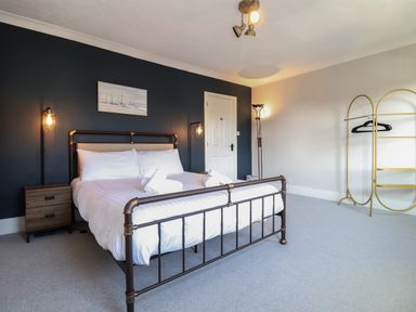 A bedroom with a metal bed frame a bedside table and a gold clothing rack at First Light in Pakefield near Lowestoft