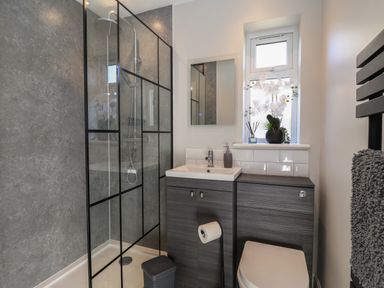 A bathroom with a walk-in shower, sink with cabinet, toilet, window with plants, and a towel rack at First Light in Pakefield near Lowestoft