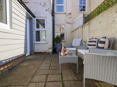 A patio area with wicker chairs a table with a bottle and glass and a potted plant at First Light in Pakefield near Lowestoft
