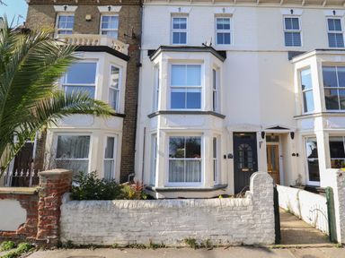 Exterior view of a white terraced house with a black front door and bay windows with a white brick wall and small garden in front at First Light in Pakefield near Lowestoft