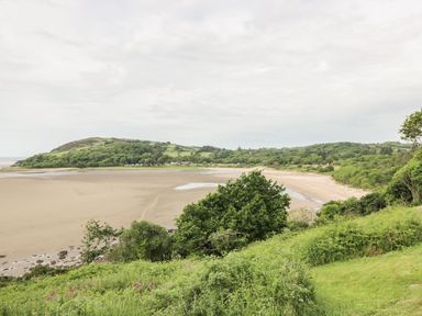 A view of a sandy beach with a river estuary and green hills in the background at Thistle Dubh Doo in Sandyhills