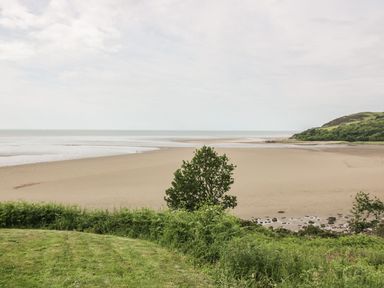 A sandy beach with sea and greenery in the foreground and hills in the background at Thistle Dubh Doo in Sandyhills