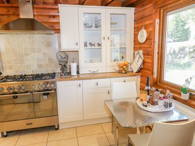 A kitchen with a gas stove white cabinets a table with chairs and a window at Thistle Dubh Doo in Sandyhills