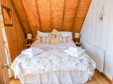 A bedroom with a bed and pillows under a wooden slanted ceiling at Thistle Dubh Doo in Sandyhills