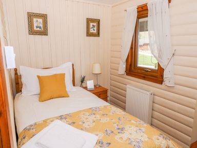 A small bedroom with a single bed white and yellow bedding wooden nightstand and window with curtains at Thistle Dubh Sandyhills