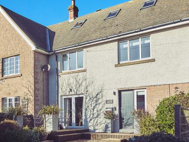 The exterior of a two story house with a wooden door and large windows at Craster Reach in Craster
