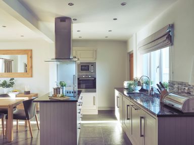 A kitchen with white cabinets black countertops built in oven and microwave and a dining table with black chairs at Craster Reach in Craster