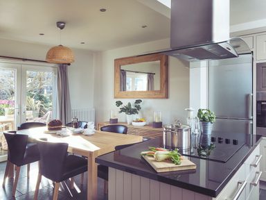 A kitchen with a wooden dining table set with a cake and cups and an island with a stove and cooking pot at Craster Reach in Craster