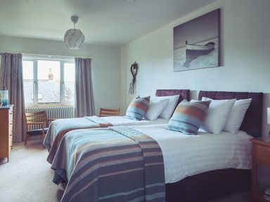 A bedroom with two twin beds with striped blankets and pillows a wooden dresser two chairs and a window at Craster Reach in Craster