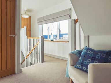A staircase landing with a window a vase with branches a white chair with a blue cushion and a wooden door at Craster Reach in Craster