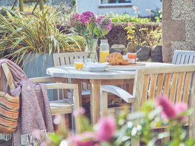 An outdoor wooden dining table with wooden chairs set with bread juice and flowers at Craster Reach in Craster