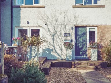 Front entrance of a house with a dark door two planters with flowers gravel driveway and outdoor seating area at Craster Reach Craster