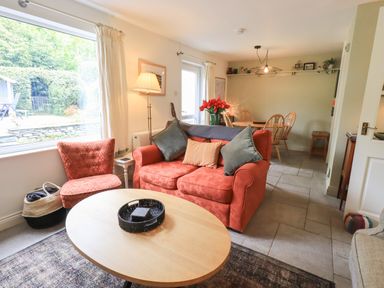 A living room with an orange sofa and chair next to a wooden coffee table and a dining table in the background at Little Hallgarth in Keswick
