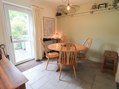 A dining area with a round wooden table and four chairs near a glass door at Little Hallgarth in Keswick