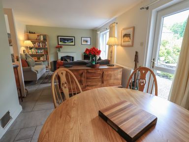 A living and dining room with a round wooden table and chairs a sofa a bookshelf and a wooden cabinet with red flowers at Little Hallgarth in Keswick
