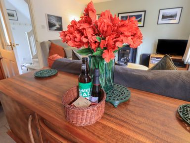 A wooden table with a wicker basket holding two bottles and a glass vase with red flowers in a living room at Little Hallgarth in Keswick