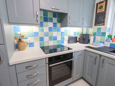 A kitchen corner with a stove oven utensil holder air fryer and cleaning supplies at Little Hallgarth in Keswick