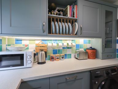 A kitchen countertop with a microwave kettle toaster jars and hanging mugs at Little Hallgarth in Keswick