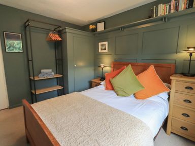 A bedroom with a double bed with orange and green pillows and wooden furniture at Little Hallgarth in Keswick