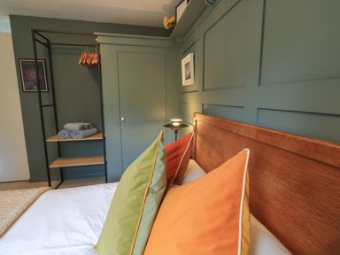 A bedroom with a wooden headboard colorful pillows a bed a black metal shelf with towels and hangers and green paneled walls at Little Hallgarth in Keswick