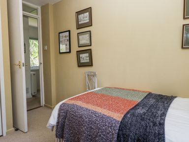A bedroom with a bed covered with a multicolored blanket a white chair and framed pictures on the wall at Little Hallgarth in Keswick