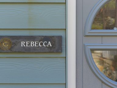 A nameplate reading Rebecca mounted on a blue wooden wall next to a gray door with a window at Rebecca in Mullion Cove near Mullion