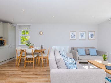 A living room and dining area with grey sofas blue cushions wooden dining table and chairs and framed pictures on the wall at Rebecca in Mullion Cove near Mullion