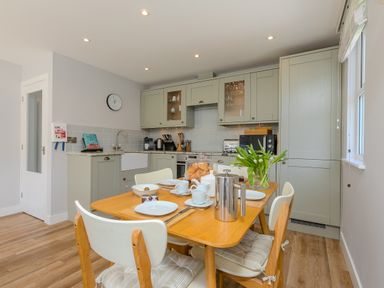 A kitchen with wooden dining table set for breakfast and green cabinets at Rebecca in Mullion Cove near Mullion