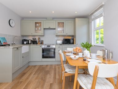 A kitchen with light gray cabinets wooden dining table set with cups plates and tulips at Rebecca Mullion Cove near Mullion