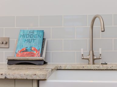 A kitchen sink with a silver faucet and a cookbook on a stand on a marble countertop