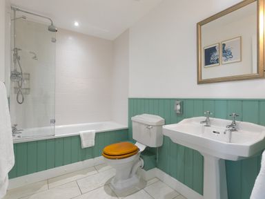 A bathroom with a bathtub shower toilet with wooden seat and a sink with mirror at Rebecca in Mullion Cove near Mullion