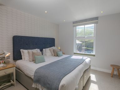 A bedroom with a double bed with a blue headboard and pillows near a window with a view at Rebecca in Mullion Cove near Mullion