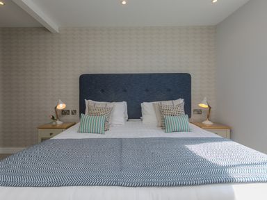 A bedroom with a bed with a blue headboard and patterned pillows at Rebecca in Mullion Cove near Mullion