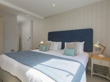 A bedroom with a double bed blue headboard bedside tables and lamps at Rebecca Mullion Cove near Mullion