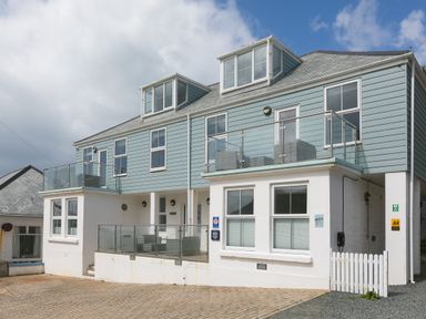 A two-story building with blue siding and white lower walls with balconies and outdoor seating at Rebecca Mullion Cove near Mullion