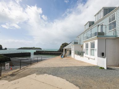 A waterfront area with a paved walkway and a blue and white building overlooking the sea at Rebecca in Mullion Cove near Mullion