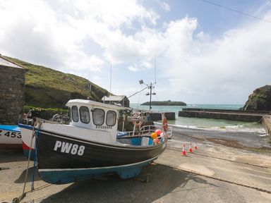 A fishing boat on a concrete slipway near a stone building with grassy hills and ocean in the background at Rebecca in Mullion Cove near Mullion