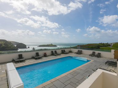 An outdoor swimming pool with loungers around on a terrace overlooking the sea at Rebecca in Mullion Cove near Mullion