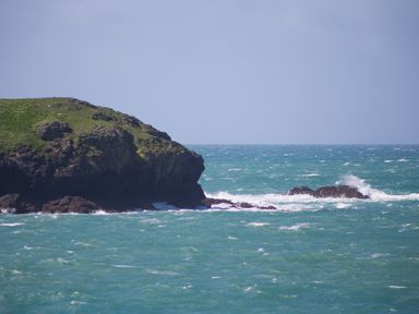 A rocky coastline with waves crashing against the rocks and green vegetation on the land at Mullion Cove near Mullion