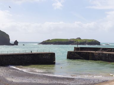 A small harbor with stone piers and a green island in the sea at Rebecca in Mullion Cove near Mullion