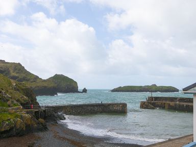 A coastal scene with stone piers extending into the sea and rocky hills in the background at Rebecca in Mullion Cove near Mullion
