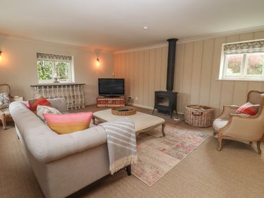 A living room with a sofa, armchairs, a wood-burning stove, a television, and a rug at Millpond Bothy in Woolhope
