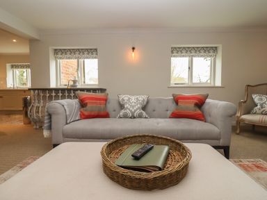 A living room with a gray sofa with patterned cushions and a wicker tray on an ottoman at Millpond Bothy in Woolhope