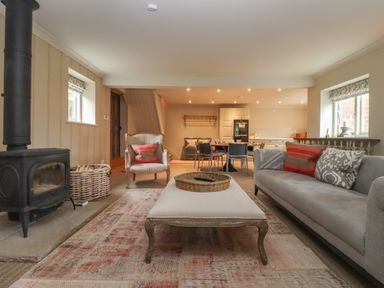A living room with a sofa armchair coffee table wood stove and dining area at Millpond Bothy in Woolhope