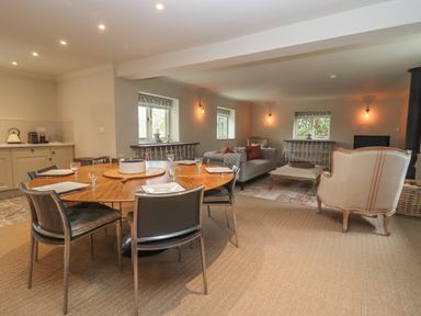 A dining area with a round wooden table and six chairs next to a living room with sofas and armchairs at Millpond Bothy Woolhope