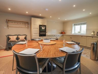 A kitchen with a round wooden dining table set with plates and glasses and cabinets along the walls at Millpond Bothy in Woolhope